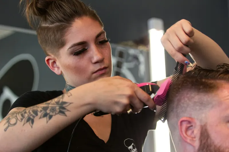 Frizeriță care tunde un client cu mașina și pieptenele