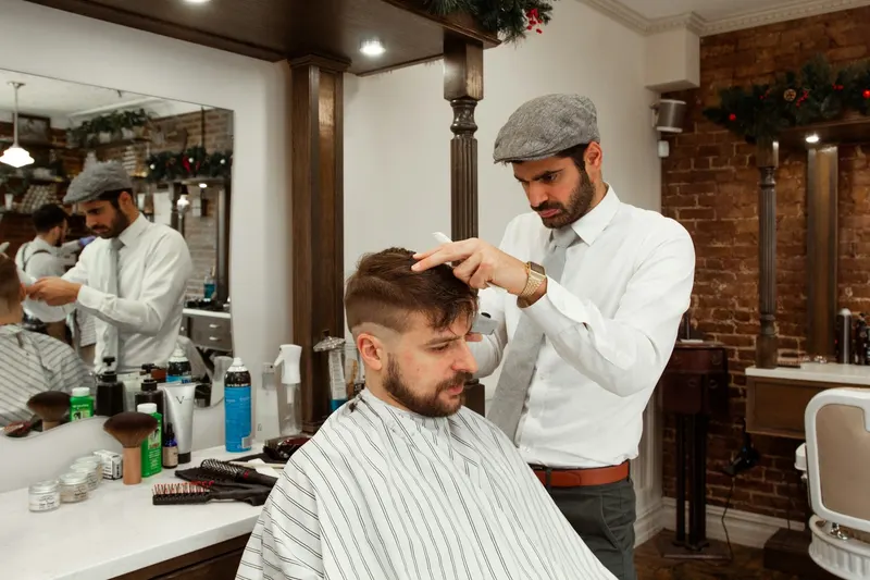 Frizer cu șapcă care aranjează părul unui client